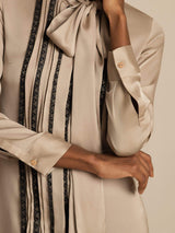 Beige silk tie-neck shirt dress with vertical pleats, lace stripe panel, and long sleeves