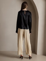 Back view of a black long sleeve silk blouse with keyhole neckline and beige wide-leg pants