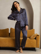 Woman wearing navy silk pajamas set with gold chain print, notch collar and piping