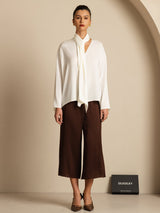White silk asymmetrical tie V-neck blouse with long sleeves, styled with brown wide-leg pants