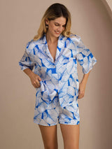 Model wearing blue leaf print silk pajama set with short sleeve button-up shirt and shorts
