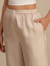 Beige high-waist silk pants with elastic waistband, button closure and side pockets