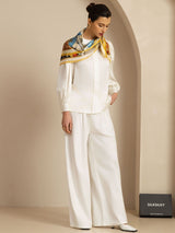 Woman wearing white silk scarf with cathedral print, paired with ivory blouse and wide-leg pants