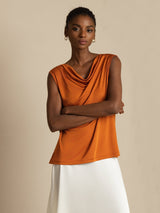 Orange sleeveless silk cowl neck top with draped front, styled with white skirt