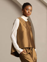 Model wearing a gold silk-wool blend vest with button pockets over a white turtleneck
