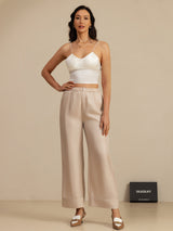 Model wearing beige high-waist full length silk pants with pockets and white crop top