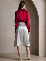 Back view of a woman wearing a red silk long sleeve lapel collar blouse with a satin midi skirt