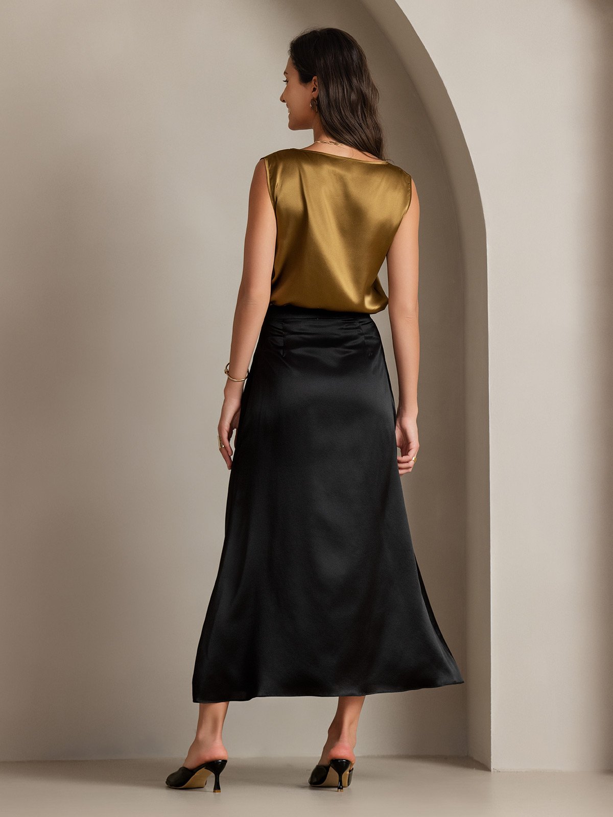 Model wearing gold sleeveless silk tank top with black midi skirt, back view