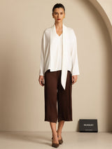 Model wearing white silk V-neck blouse with asymmetrical tie and brown wide-leg pants