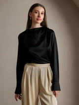 Model wears black silk long sleeve boat neck blouse with beige trousers