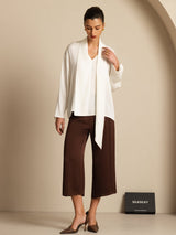 White silk asymmetrical V-neck blouse with long sleeves, styled with brown cropped pants