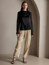 Black silk long sleeve boat neck blouse with beige pants, model wearing elegant silk top