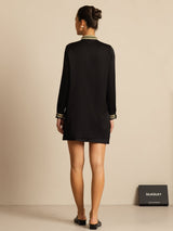Back view of black silk women's pleated stand collar blouse with contrast piping and long sleeves