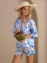 Woman wearing blue-and-white leaf print silk pajama set with short-sleeve button-up top and shorts