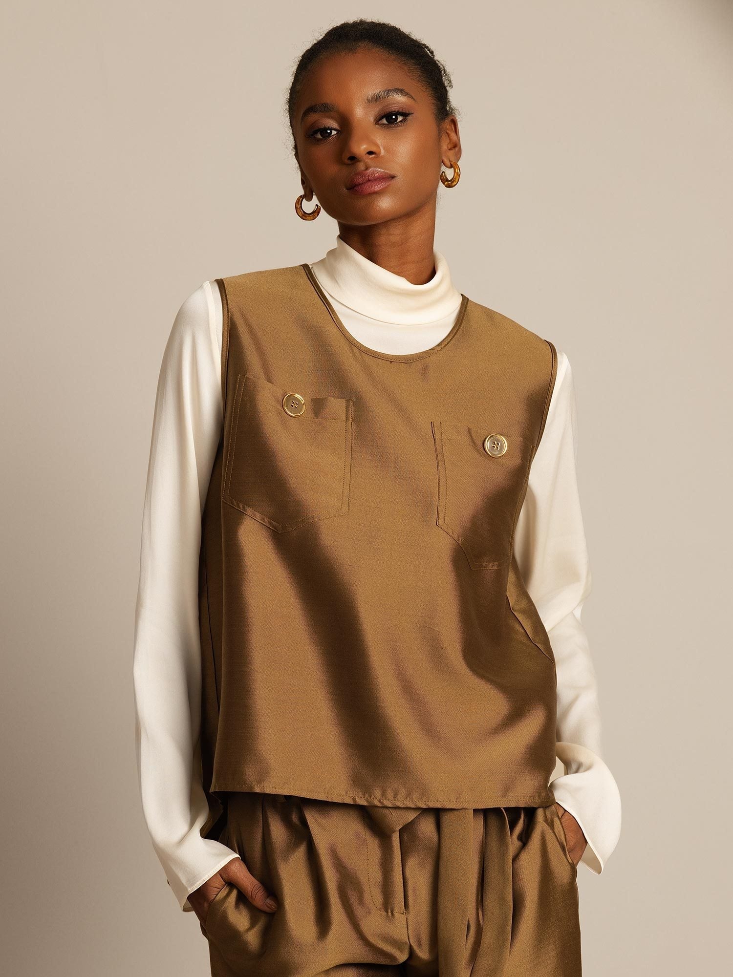 Model wearing brown silk-wool blend vest with button pockets over cream turtleneck