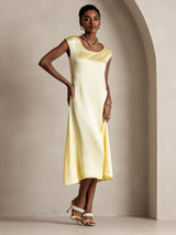 Model wearing a pale yellow silk midi dress with round neck and cap sleeves