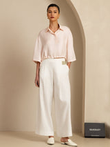 Model wearing pale pink silk cropped blouse with drawstring hem and white wide-leg trousers