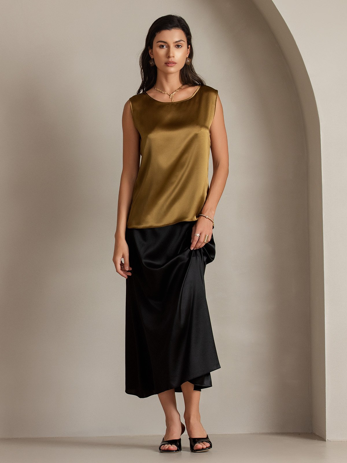 Women's silk sleeveless round neck tank top in gold, styled with black skirt
