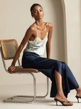 Model wearing navy silk wide leg split pants with lace camisole, seated on chair