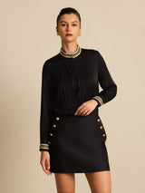 Black silk stand-collar blouse with pleats, contrast piping, and gold trim on cuffs