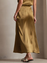 Model wearing a gold silk A-line maxi skirt with side zip and flowing bias cut